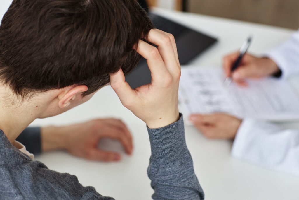 High angle troubled man scratching head during consultation with doctor